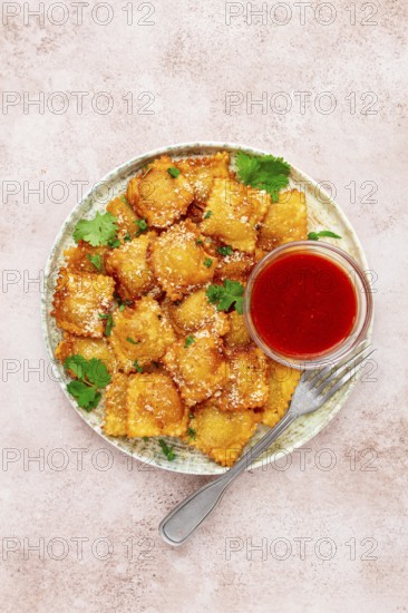 Fried ravioli with parmesan cheese, served with red sauce and garnished with herbs, on a light background, no people