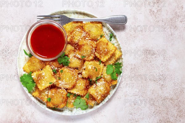 Fried ravioli with parmesan cheese, served with red sauce and garnished with herbs, on a light background, no people