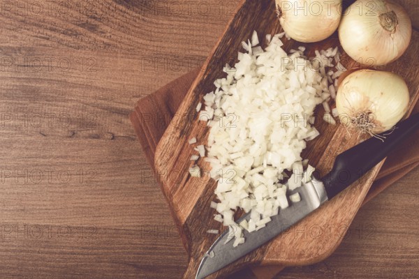 Finely chopped onion on a chopping board with a knife, wooden table, top view, no people