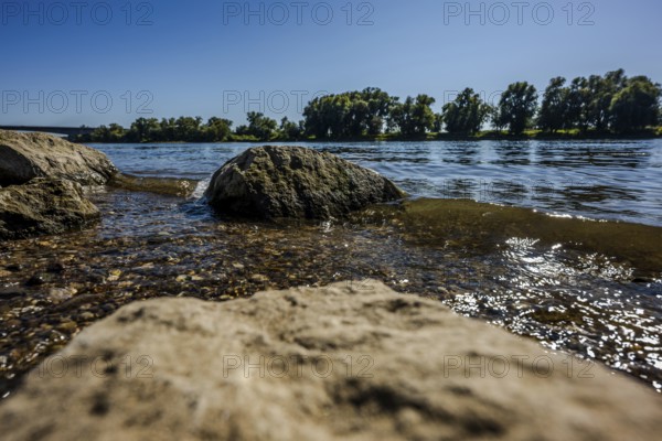 The scene shows a calm river with large stones lying on its banks. The water glistens in the sun, the landscape is green and peaceful. It is a beautiful, sunny day. Bogen, Lower Bavaria