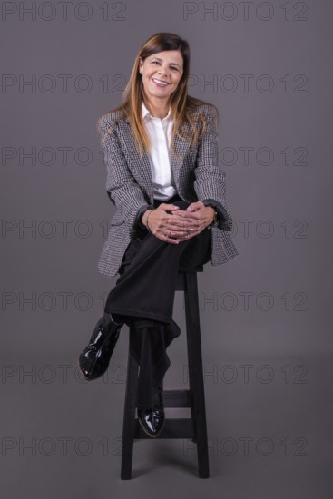 Elegant senior businesswoman sitting on a stool and smiling at the camera