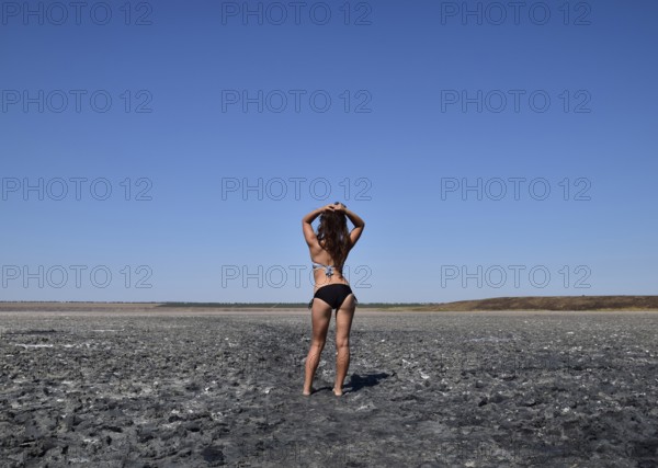 Walk the dark-haired woman in a swimsuit on the bottom of a dry lake with salt and mud. Taman, Krasnodar Krai, Russia