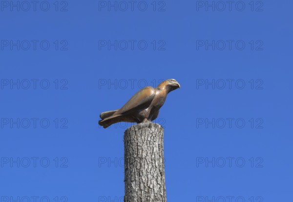 Figurine of a falcon on a stump of a tree against the blue sky. Taman, Krasnodar Krai, Russia