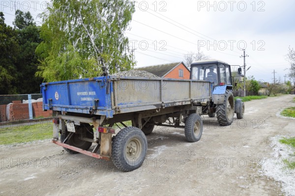 A tractor with a rubble cart for repairing the road. Feeding holes on the road. Krasnodar, Russia