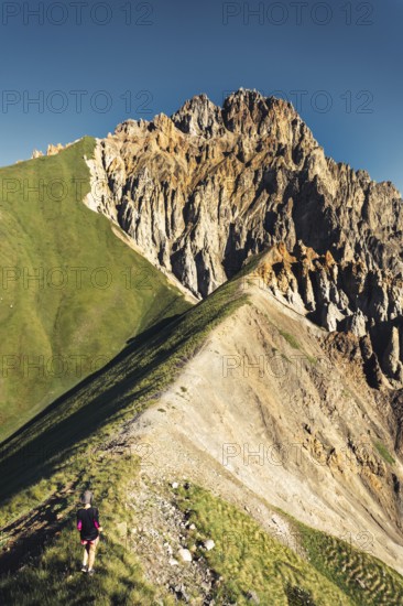 Hiker walking along narrow ridge trail at Kabarjina Mountain in Kazbegi National Park Georgia with dramatic rocky peak view