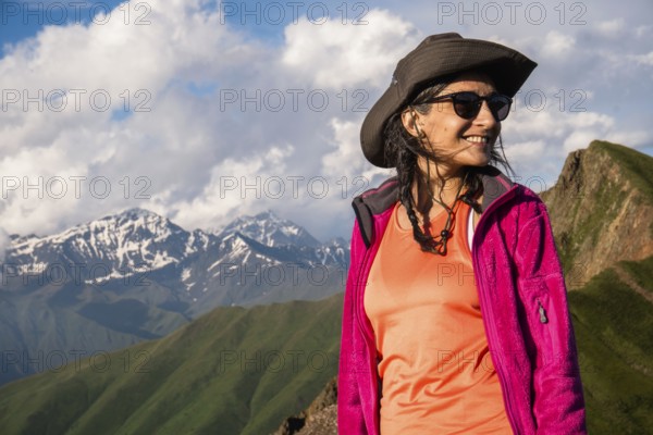 Happy Young Traveler hiker woman portrait wearing hat and jacket smiling in Kazbegi National Park mountains of Georgia, adventure lifestyle and hiking portrait