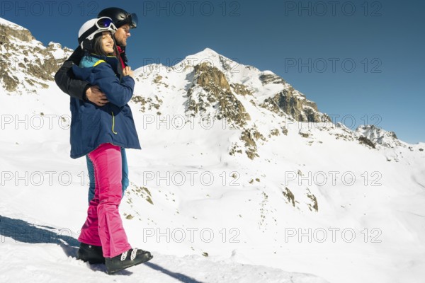 Young caucasian couple pose hug enjoying looking at snowy mountains range in winter. Get away skiing holidays lifestyle. Tetnuldi ski resort viewpoint. Caucasus mountains high altitude freeriding