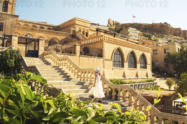 Traveler woman in white dress walking stairs of historic building - visit Mardin museum in old city of Mardin Turkey with traditional Mesopotamian architecture