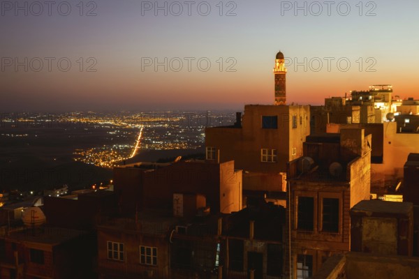 Illuminated mosque minaret above Mardin old town with glowing city lights and Mesopotamian plains at sunset. Great Mosque of Mardin Ulu Camii Minaret