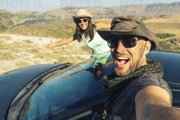 Happy young caucasian couple taking selfie while sitting in rented vehicle black car having road trip Europe. Outdoor lifestyle activity on road trip vacation concept. Excited happy couple enjoy ride