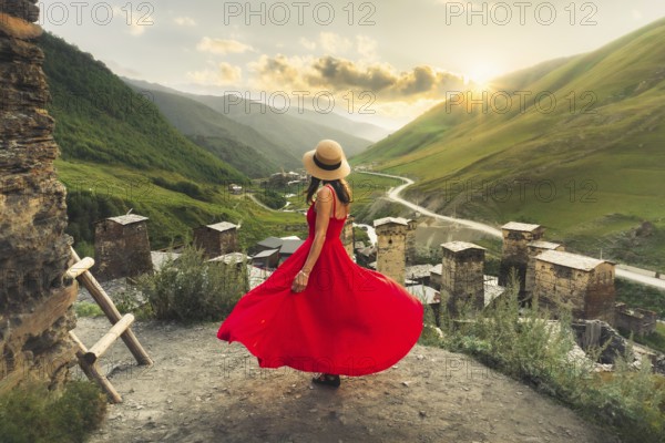 Woman in red dress looking at medieval towers of Ushguli Georgia during sunset with mountains and Enguri valley landscape