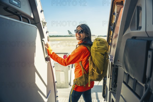 Young happy caucasian female traveler backpacker with carry on hiking backpack boarding airplane pose at aircraft entrance smiling, adventure tourism lifestyle, journey. Weekend trip get away Europe