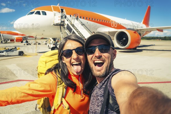 Young happy caucasian couple taking selfie portrait on departure or arrival destination for vacation on sunny autumn day. Budget student travelers, vacationist, explorers having fun. Weekend escape
