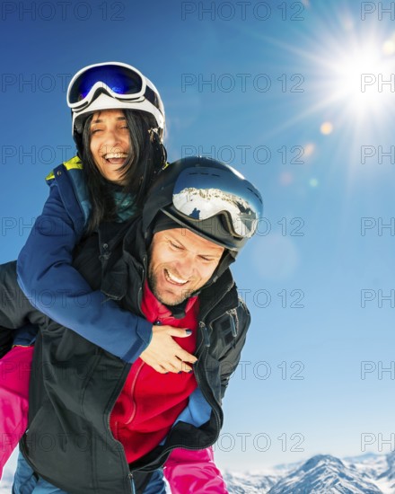 Romantic happy skiers couple in love having fun together playing in mountains piggybacking at wintertime.Winter lovers couple isolated mock up outdoors blue banner copy space background