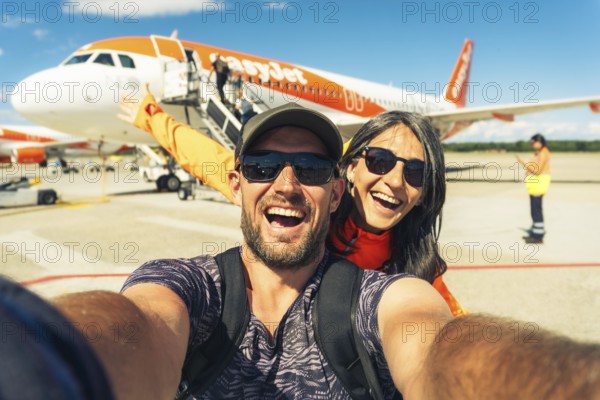 Milan, Italy - 12th august, 2025: happy smiling couple taking selfie in front of EasyJet airplane while boarding at Milan airport during summer travel adventure