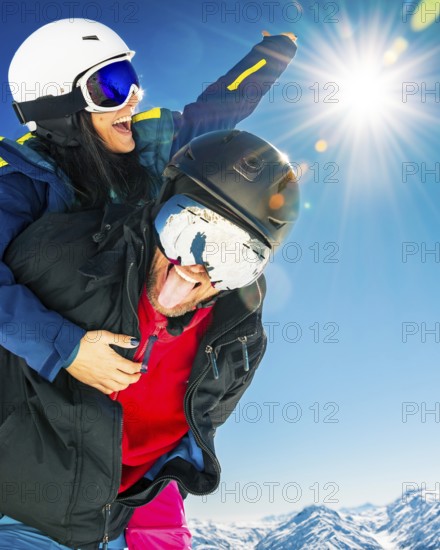 Happy young caucasian skiers couple in love having fun together playing in mountains piggybacking at wintertime. Couple ski together enjoy vacation making silly face for holiday picture outdoors
