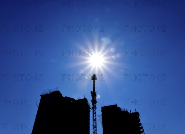 Tower crane under construction between the two high-rise buildings against the blue sky and sun. Atyrau, Kazakhstan