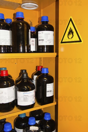 Flammable Chemicals In Bottles With Different Size in Orange Protection Cabinet, Marked With A Flammable Warning Sign