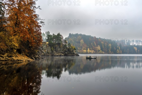 Foggy Landscape With Fishermans Boat On Calm Lake And Autumnal Forest At Lake Ottenstein In Austria