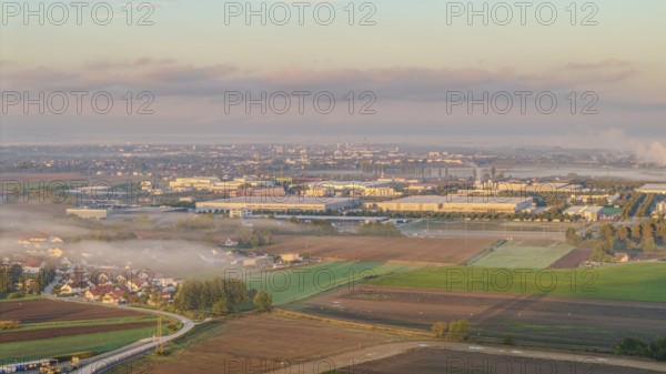 An extensive industrial area becomes visible in the morning sun. Fog envelops the landscape and the silhouettes of the buildings, while the first rays of sunlight shine. Straubing harbour, Lower Bavaria