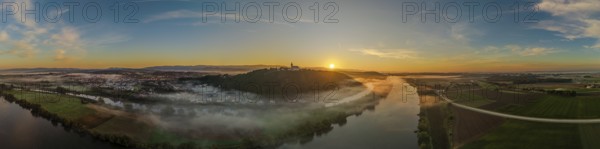 The sunrise shines over the Danube valley. Mist hovers over the river, while the rolling hills and the city become visible in the background. A beautiful sight. Bogen, Lower Bavaria