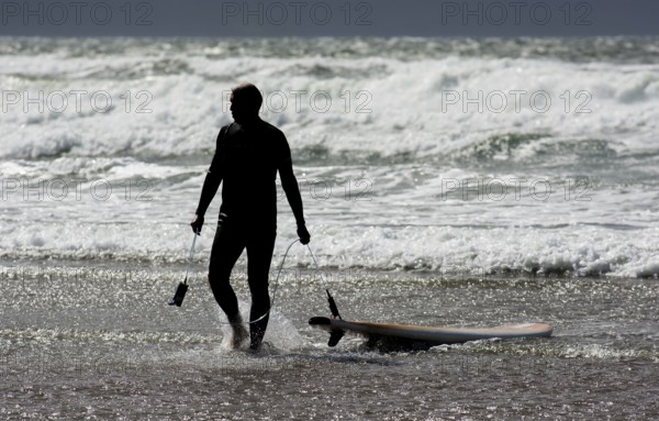Silhouette Of A Surfer With His Surfboard Leaving Water Of Cold Atlantic At The Coast Of Ireland