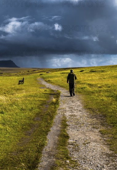 Old Man With Walking Stick Strolls On Narrow Gravel Path Through Scenic Landscape With Spectacular Clouds In Scotland, United Kingdom