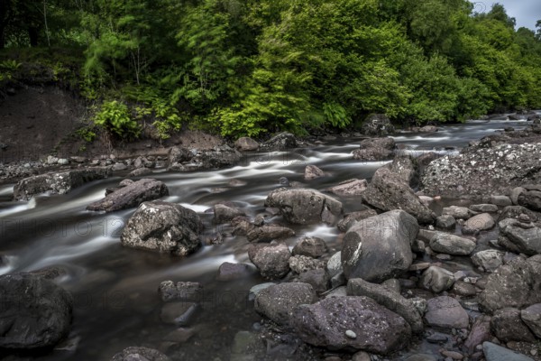 Long-Time Exposed Wild Mountain River Streaming Through Green Forest in Scotland, United Kingdom