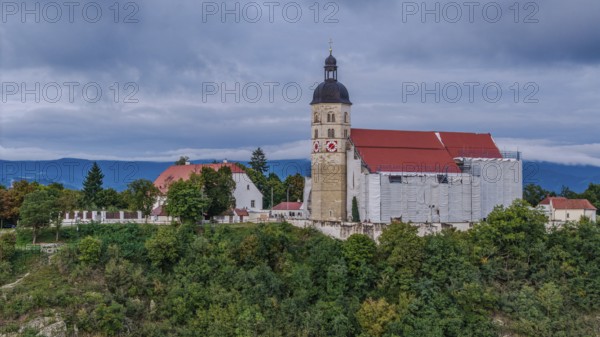 The pilgrimage church of the Assumption of the Virgin Mary on the Bogenberg is surrounded by scaffolding during its renovation. Gentle hills and a cloudy sky are visible in the background. Bogen, Lower Bavaria
