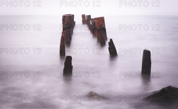 Wooden bridge remains in silky water with sea horizon in the background. Concept of time and tranquility. Taken in Odesa waterfront. Ukraine