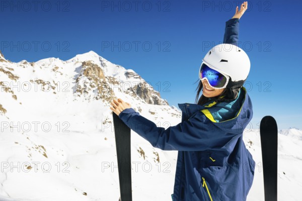 Young happy caucasian woman pose with skis looking at camera hands up in alpine zone. Get away skiing holidays lifestyle. Caucasus mountains top pristine high altitude freeriding concept