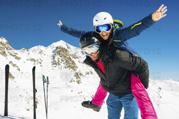 Happy caucasian skiers couple in love having fun arms outstretched together playing in mountains piggybacking at wintertime. Couple ski isolated mock up outdoors blue banner copy space background