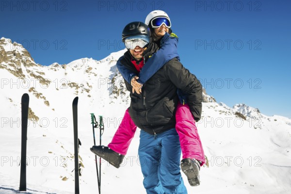 Happy young caucasian adult skiers couple in love having fun together playing enjoy leisure mountains piggybacking at wintertime. Couple ski isolated outdoors blue winter ski ad banner background