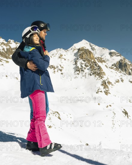 Young caucasian couple pose hug enjoying looking at snowy mountains range in winter. Get away skiing holidays lifestyle. Tetnuldi ski resort viewpoint. Caucasus mountains high altitude freeriding