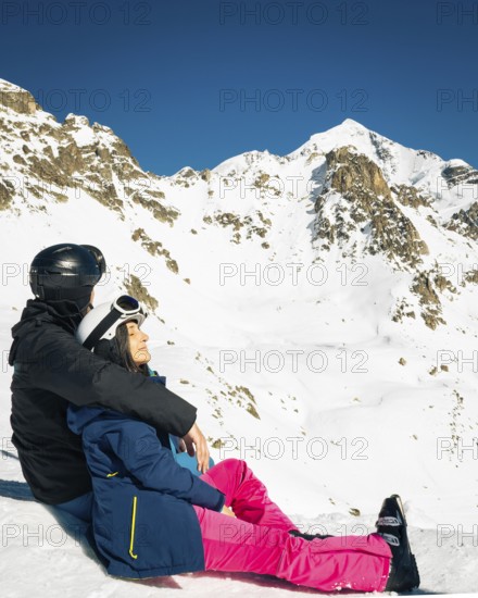 Young caucasian couple pose sits hug enjoying looking at snowy mountains in winter. Get away skiing holidays lifestyle. Tetnuldi ski resort viewpoint. Caucasus mountains high altitude freeriding