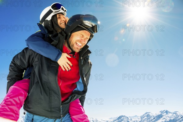 Couple skiers piggyback having fun hugs enjoy winter holidays outdoors in ski resort with eyes closed. Face skin eye protection in high snowy alpine mountains
