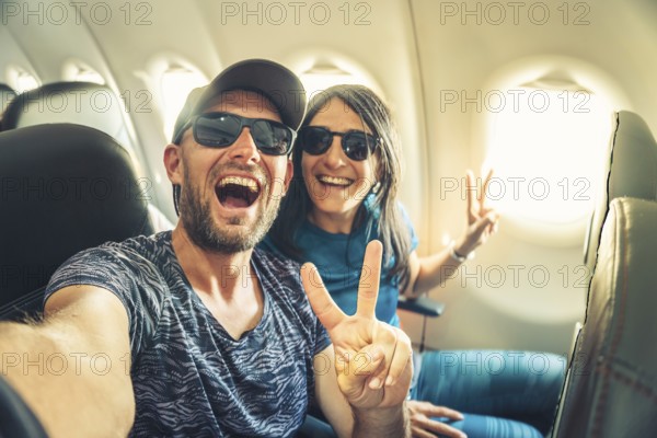 Smiling couple taking selfie inside airplane during flight, showing joy, freedom and travel lifestyle concept