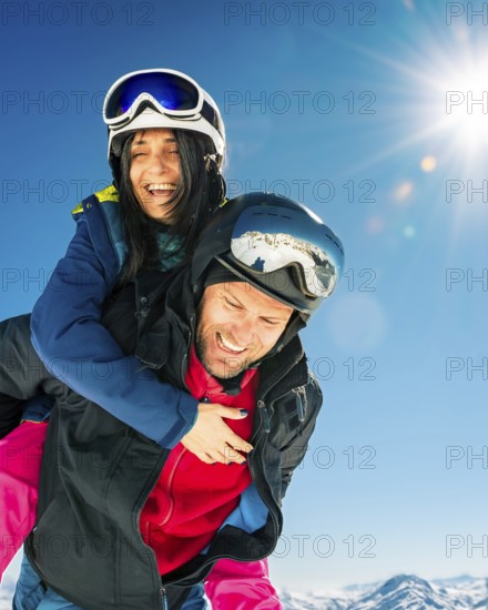 Happy young caucasian adult skiers couple in love having fun together playing enjoy leisure mountains piggybacking at wintertime. Couple ski isolated outdoors blue winter ski ad banner background