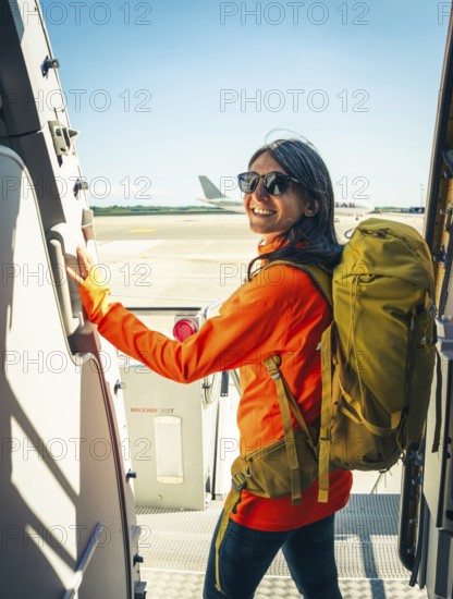 Young happy caucasian female traveler backpacker with carry on hiking backpack boarding airplane pose at aircraft entrance smiling, adventure tourism lifestyle, journey. Weekend trip get away Europe