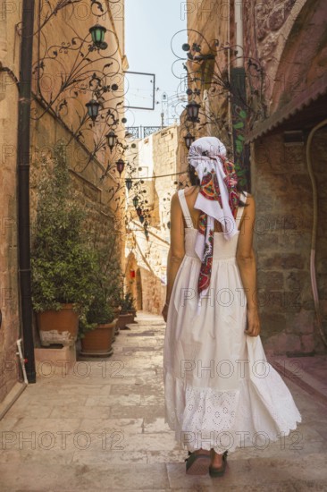 Traveler woman in white dress walking through narrow stone alley in historic city of Mardin Turkey with traditional architecture