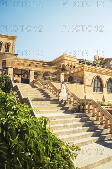 Traveler woman in white dress walking stairs of historic building - visit Mardin museum in old city of Mardin Turkey with traditional Mesopotamian architecture