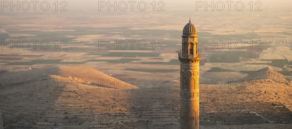 Historic Ulu Cami mosque minaret in Mardin Turkey illuminated by sunset against vast Mesopotamian plains and Anatolian landscape