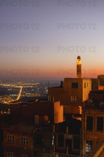 Illuminated mosque minaret above Mardin old town with glowing city lights and Mesopotamian plains at sunset. Great Mosque of Mardin Ulu Camii Minaret