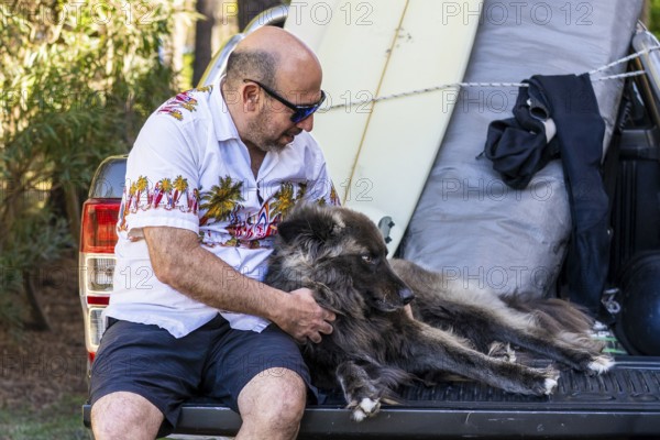 A man with a dog and surfboards sitting on the back of a truck