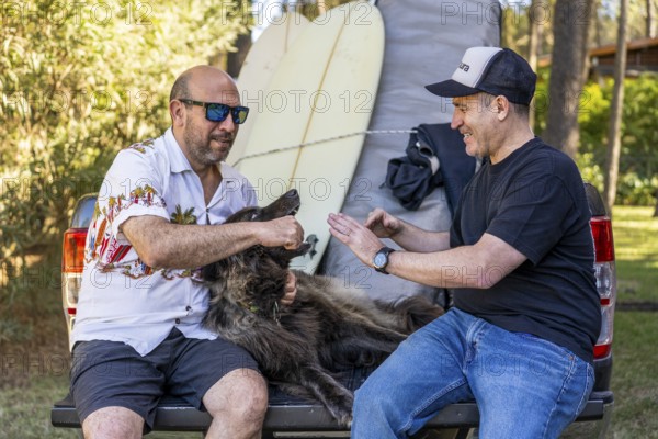Two men and their dog relaxing on a pickup truck