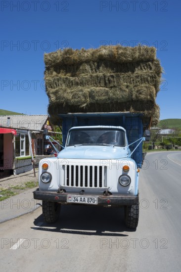 A blue lorry loaded with several layers of hay bales is parked on a country road, Armenia