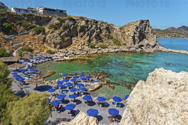 Grande Blue Beach with many blue parasols in front of a rocky coast and clear blue sea, Grande Blue Beach, Stegna, Archangelos, Rhodes Island, Greece