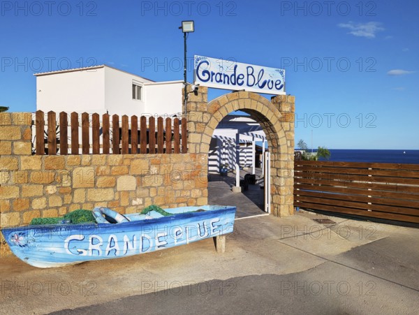 Exterior view of the Grande Blue Restaurant on the coast with a decorative boat and a stone entrance gate, Grande Blue Beach, Stegna, Archangelos, Rhodes Island, Greece