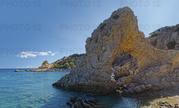 Grande Blue coast with a natural stone arch in front of clear blue water under a sunny sky, Grande Blue Beach, Stegna, Archangelos, Rhodes Island, Greece