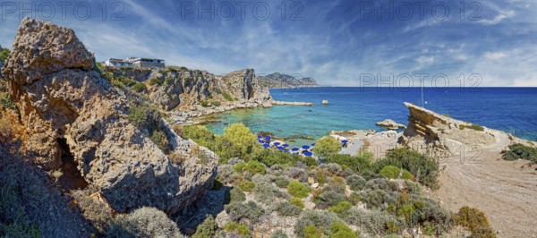Rocky coastal landscape Grande Blue with clear blue sea and blue sky, lined with parasols on the beach, Grande Blue Beach, Stegna, Archangelos, Rhodes Island, Greece